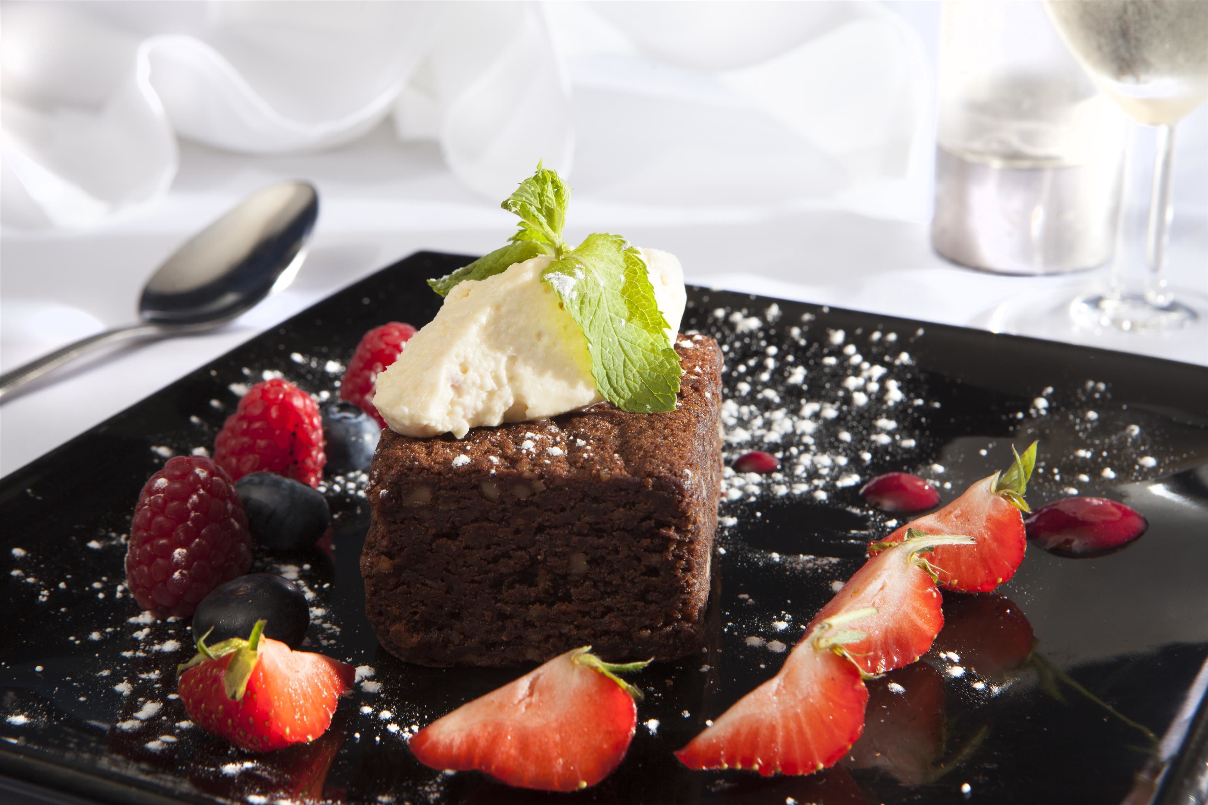 A dessert with chocolate cake, ice cream, and berries on a black plate.