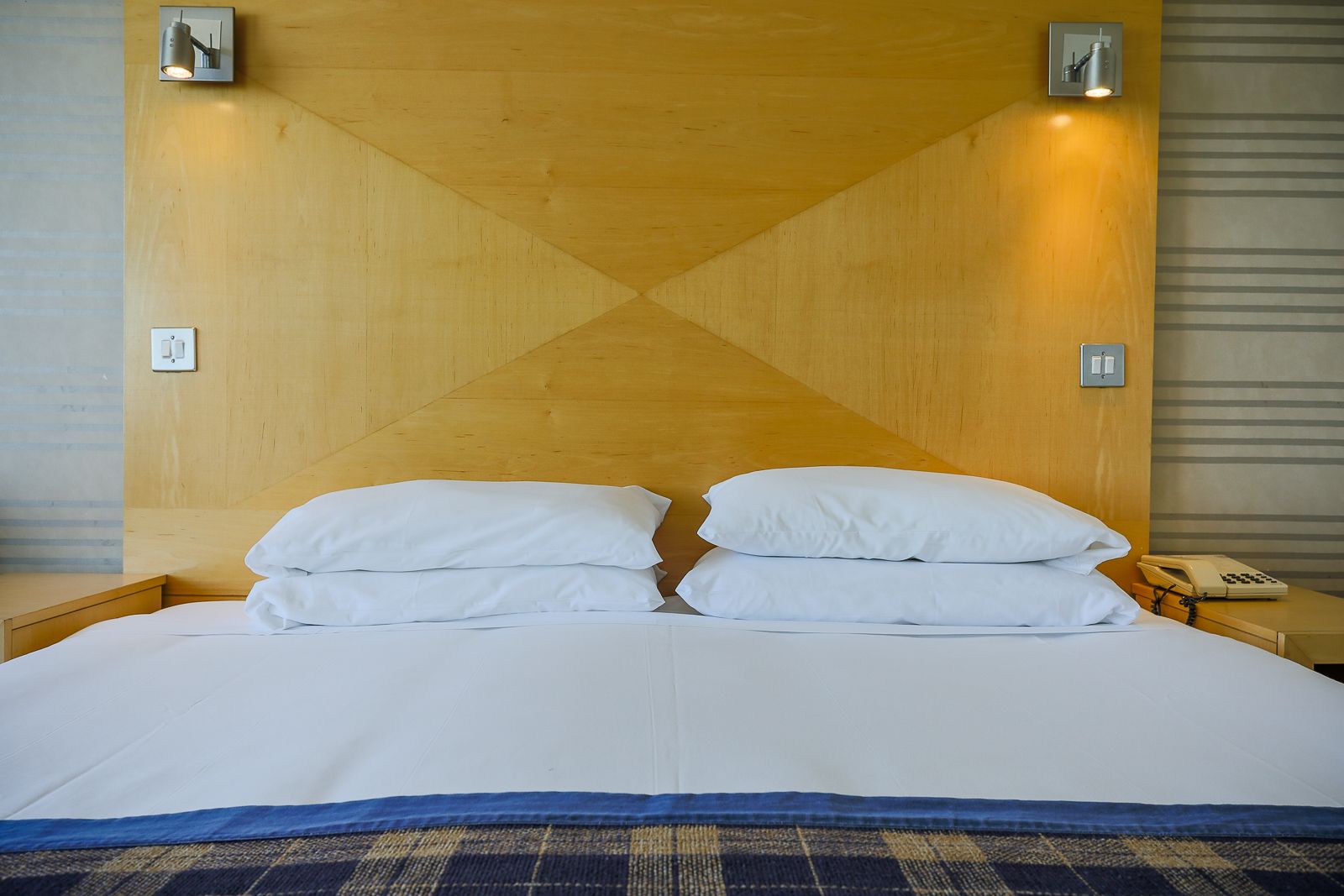 Ein Hotelzimmer mit einem großen Bett, zwei Nachttischen, einem Telefon und Wandleuchten.