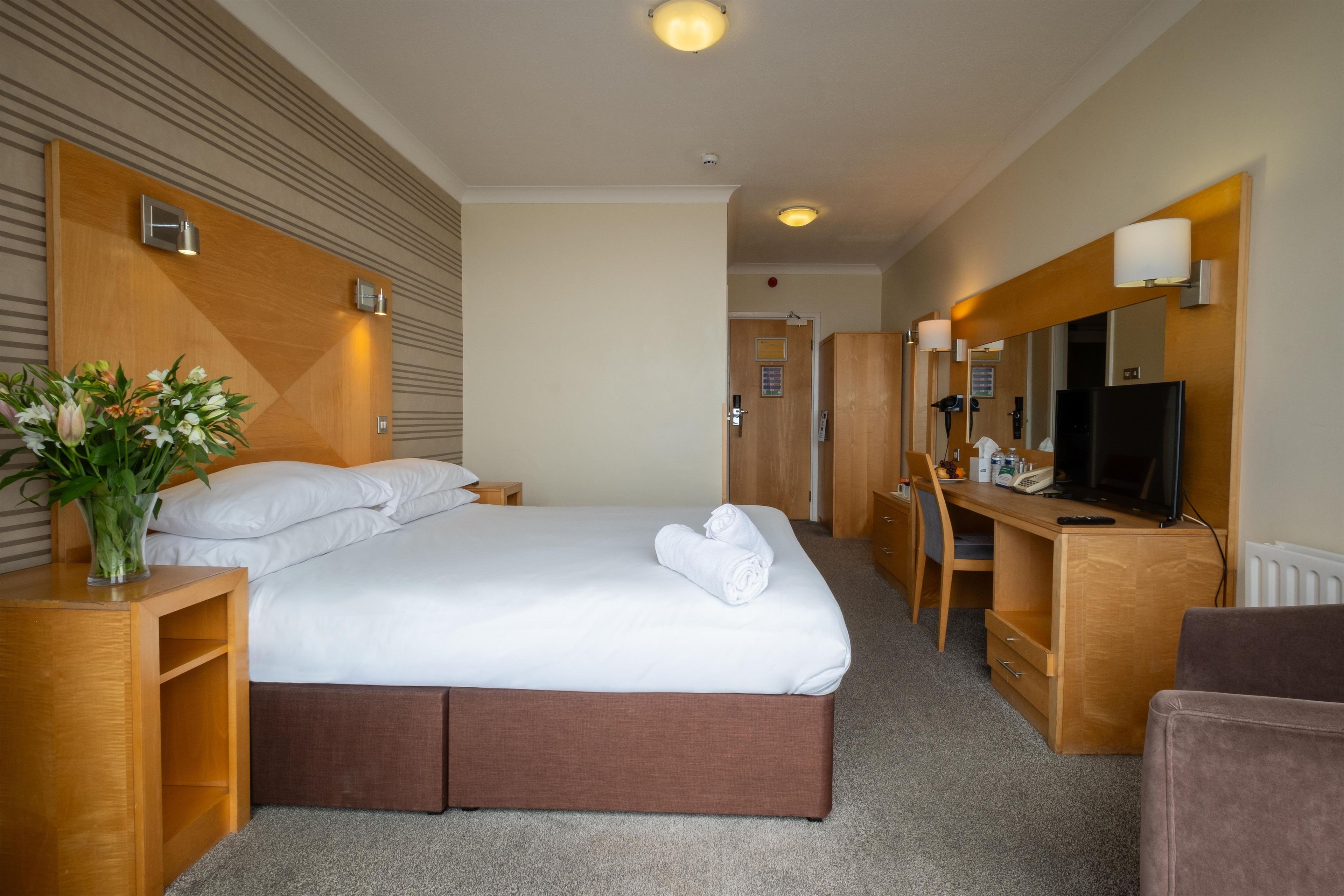 A hotel room with a bed, a desk, a chair, a television, and a mirror.