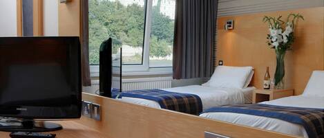 Une chambre d’hôtel équipée d’une télévision, de tables de chevet, d’un miroir et d’une fenêtre avec des rideaux.