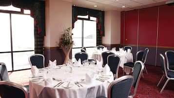 Un salón de conferencias con mesas redondas dispuestas para una reunión, ventanas amplias con cortinas y una pared roja.