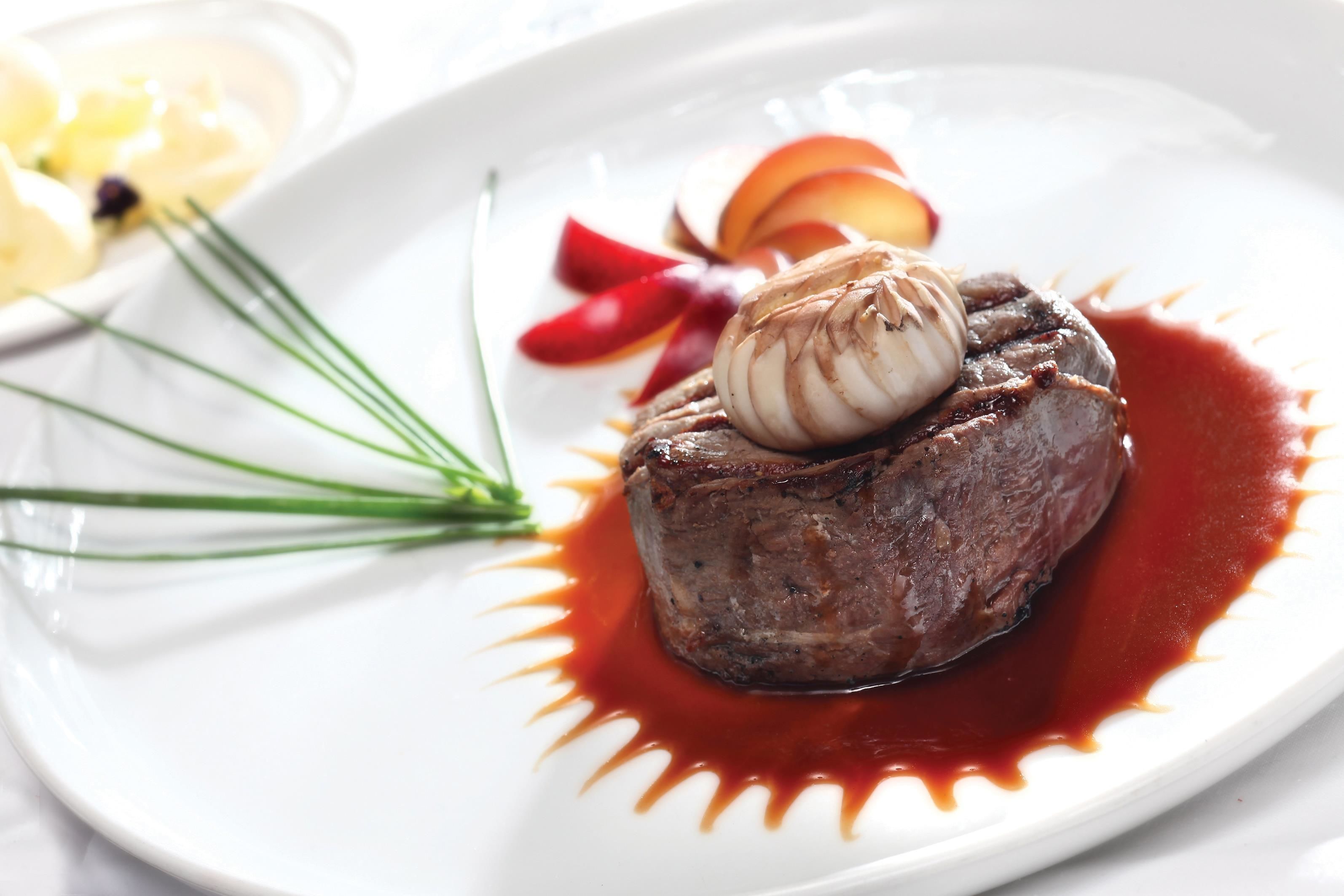 A steak with a garnish of chives and a red sauce on a white plate.