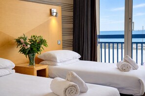 A hotel room with two beds, a nightstand with a vase of flowers, and a view of the sea through a balcony. - Best Western Palace Hotel & Casino (Douglas)