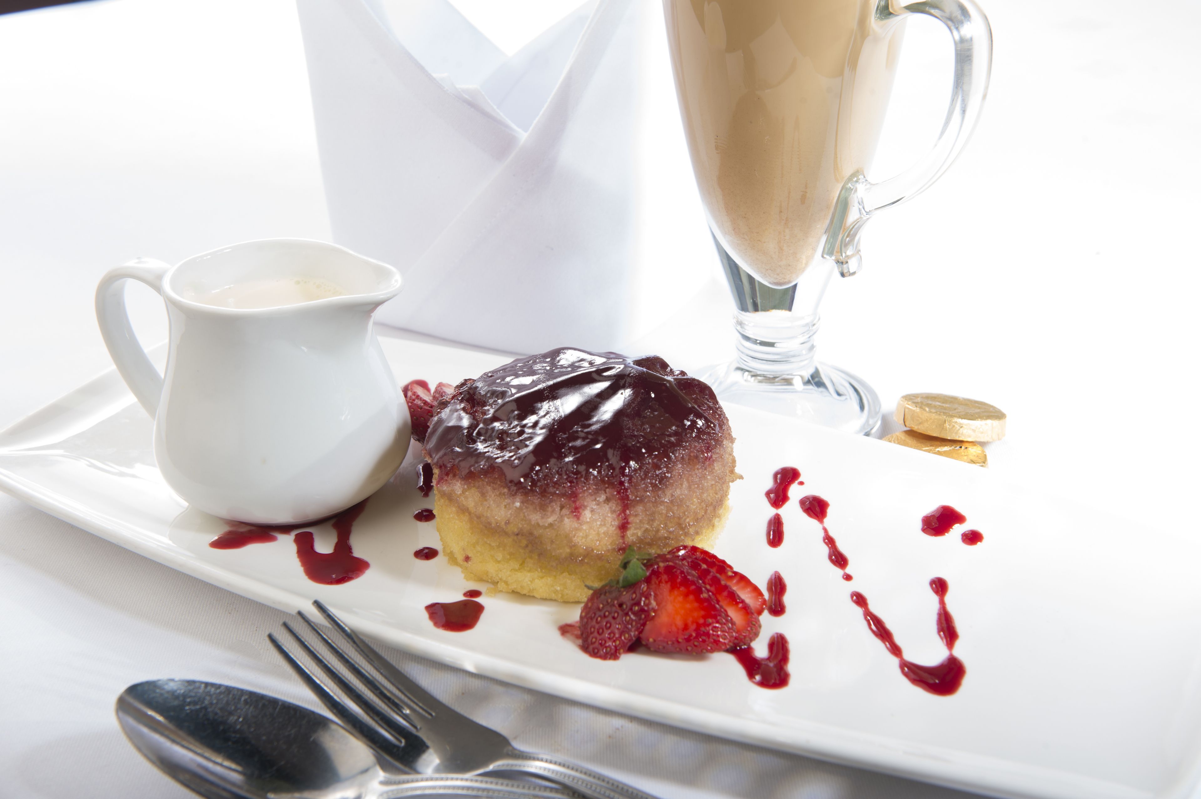Un plato de postre con pastel, fresas y una pequeña jarra de salsa.