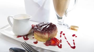 A dessert plate with a cake, strawberries, and a small jug of sauce.