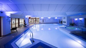 Una piscina interior con agua cristalina, un trampolín y sillas de descanso.