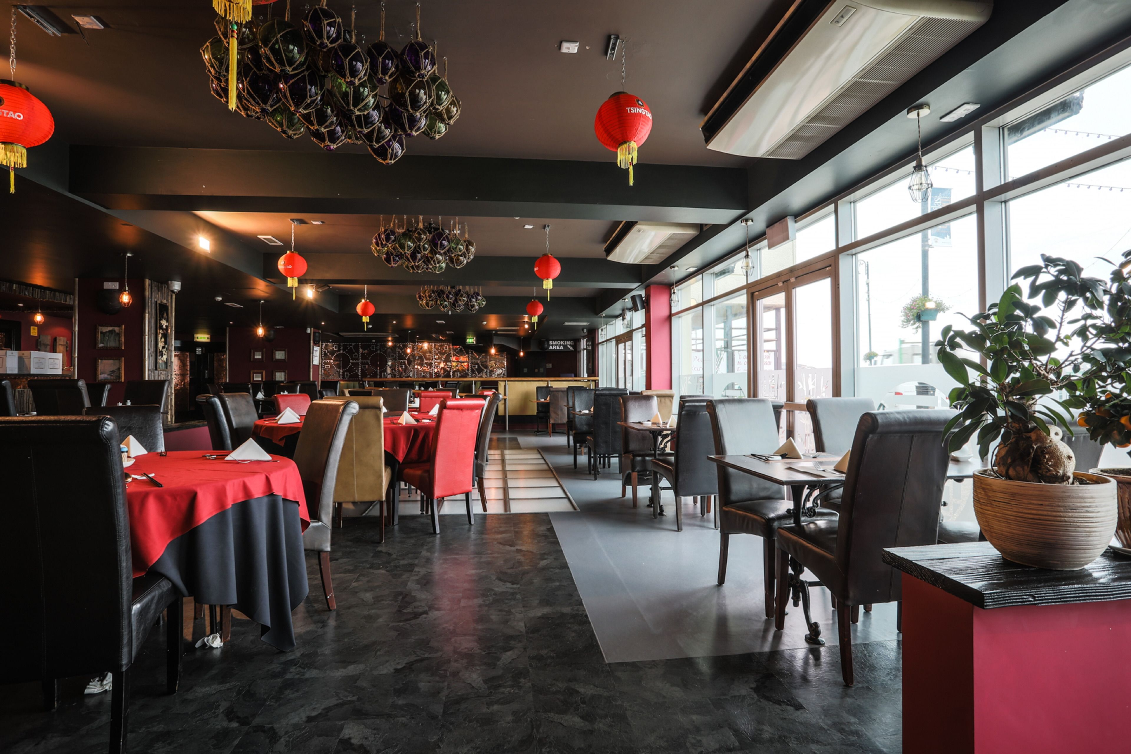 A restaurant with tables and chairs, red lanterns, and a large window.