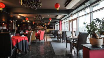 A restaurant with tables and chairs, red lanterns, and a large window.