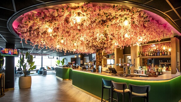 Una zona de bar con un mostrador verde, taburetes y un techo decorado con flores rosadas.