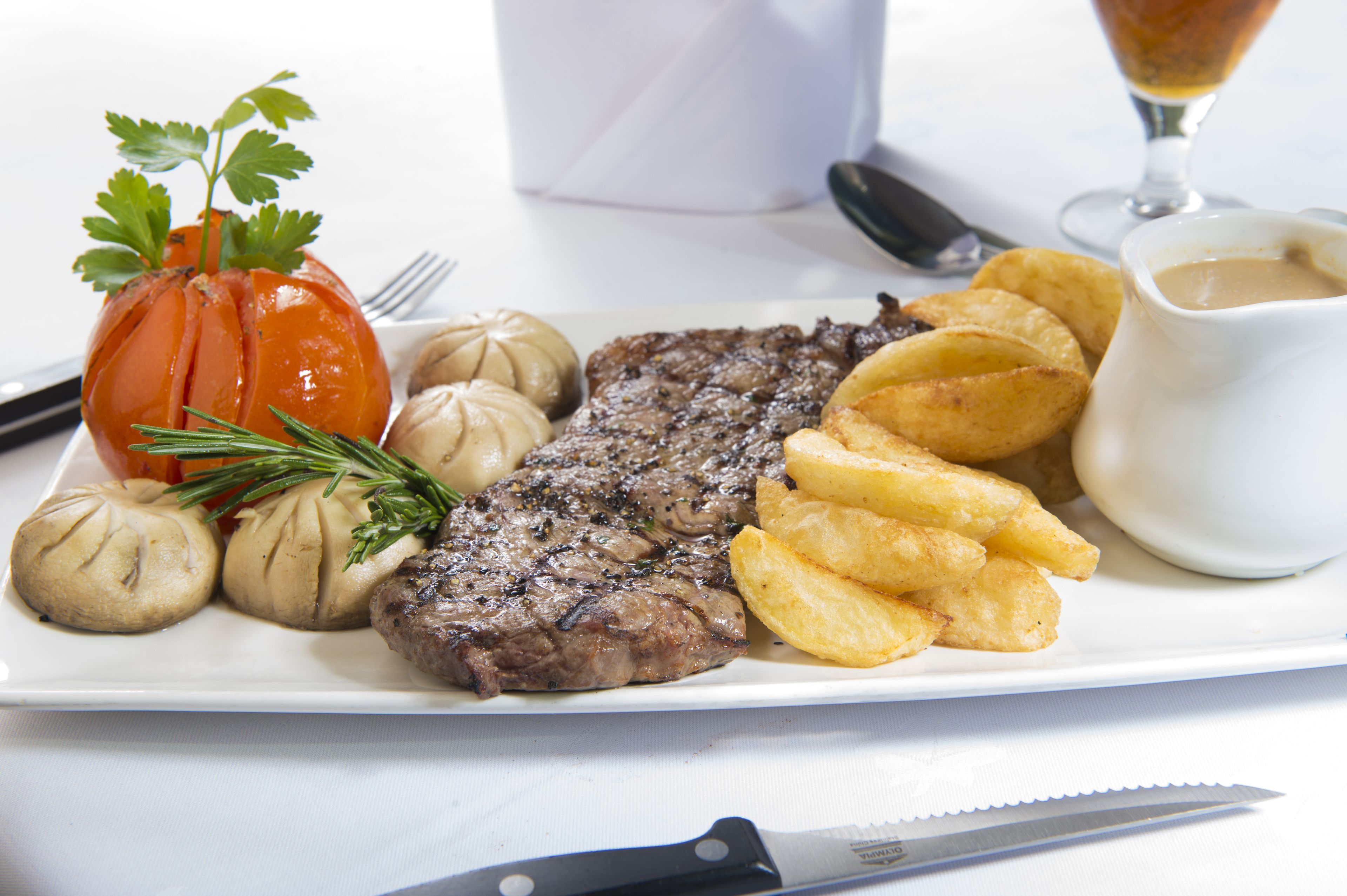 A plate with steak, potatoes, and a small tomato.