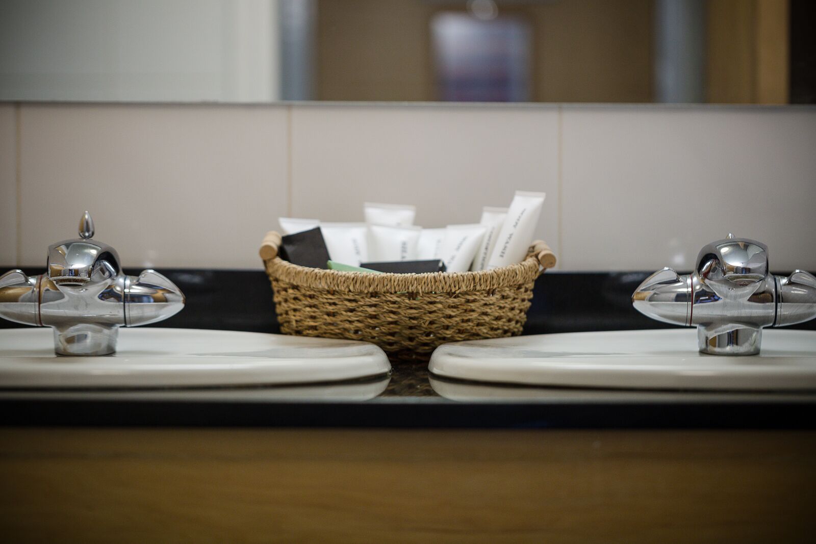 A bathroom with two sinks, a woven basket between them, and a mirror reflecting the room.