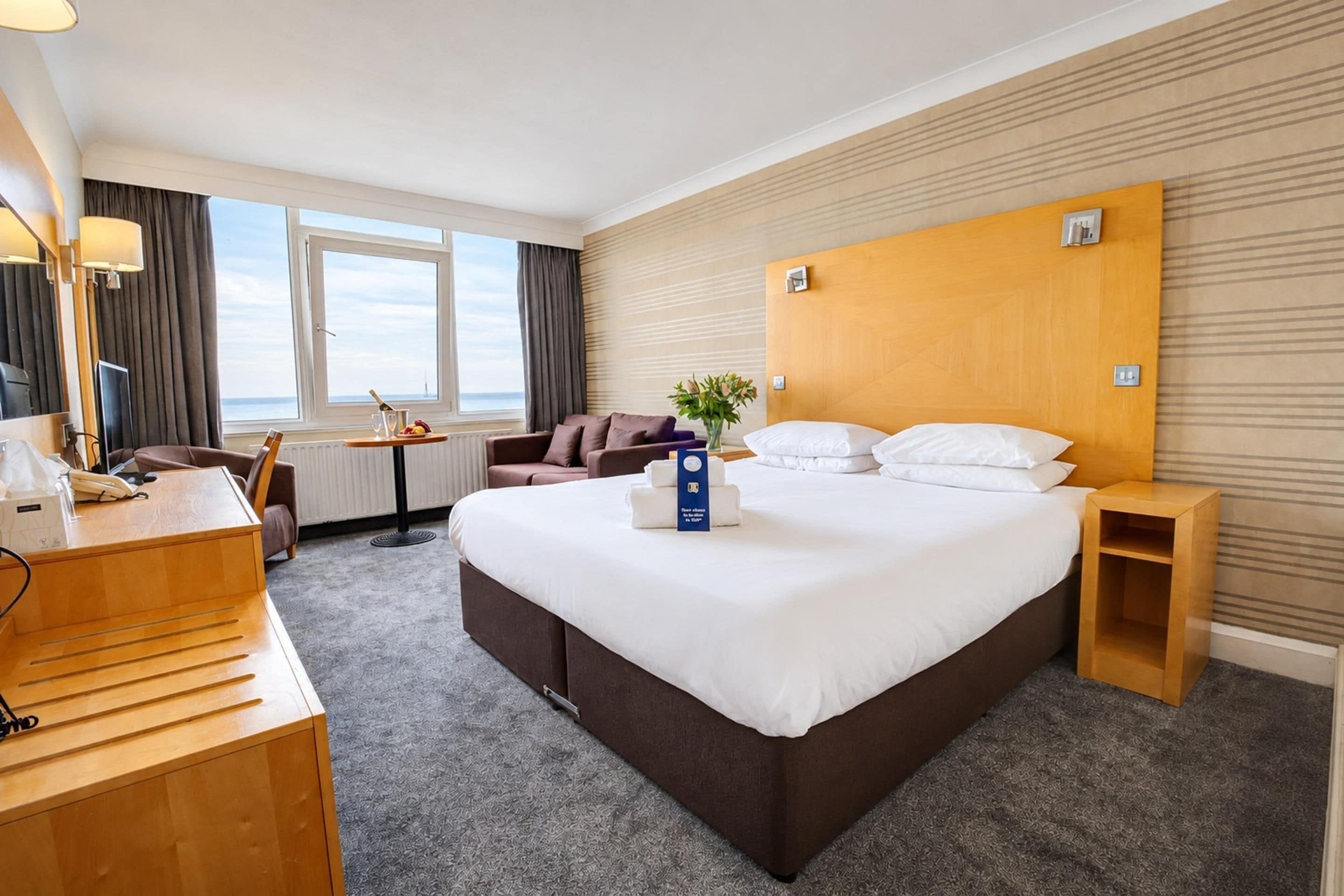 A hotel room with a large bed, a desk, a chair, a sofa, and a view of the sea.