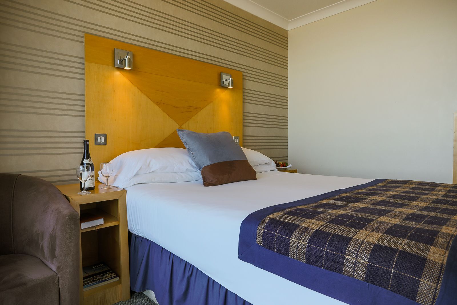 Une chambre d’hôtel avec un lit, une table de chevet, une bouteille de vin et un magazine.