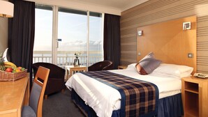 Habitación de hotel con cama, escritorio, silla, una mesita y vistas al exterior.