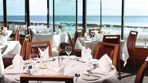 Comedor con mesas dispuestas para una comida, con vistas a la costa.