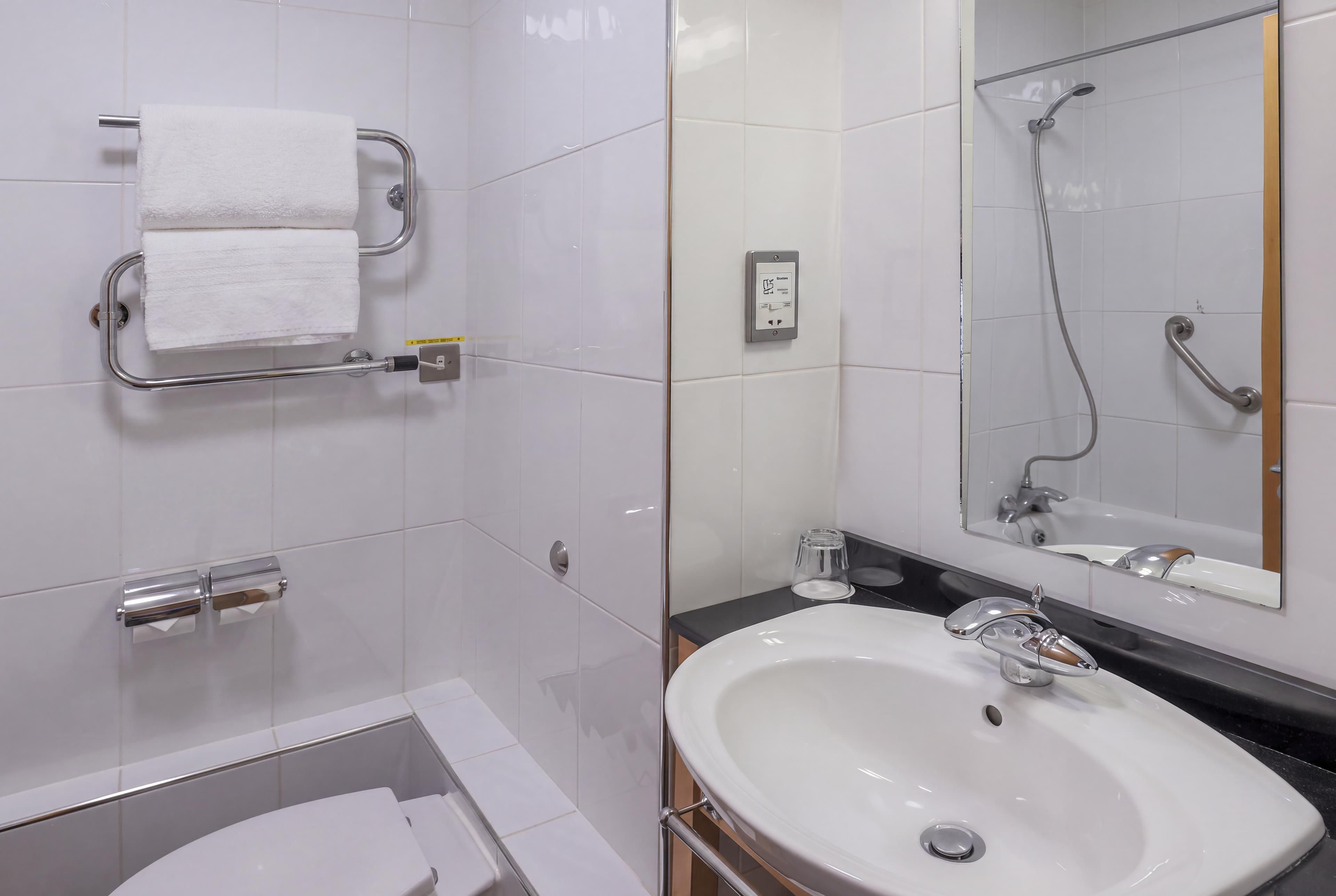 A modern bathroom with a white sink, a mirror, a towel rack, and a shower.
