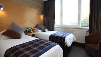 Habitación de hotel con dos camas, cabecera de madera, ventana con cortinas y una silla.