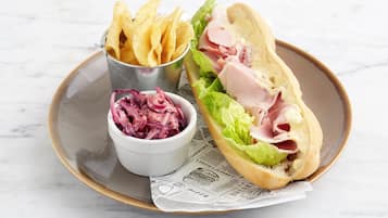 A sandwich with lettuce and ham, a small bowl of red cabbage, and a container of chips on a plate.