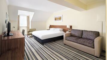 A hotel room with a bed, a sofa, a desk, and a television.