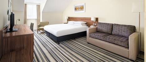 A hotel room with a bed, a sofa, a desk, and a television.