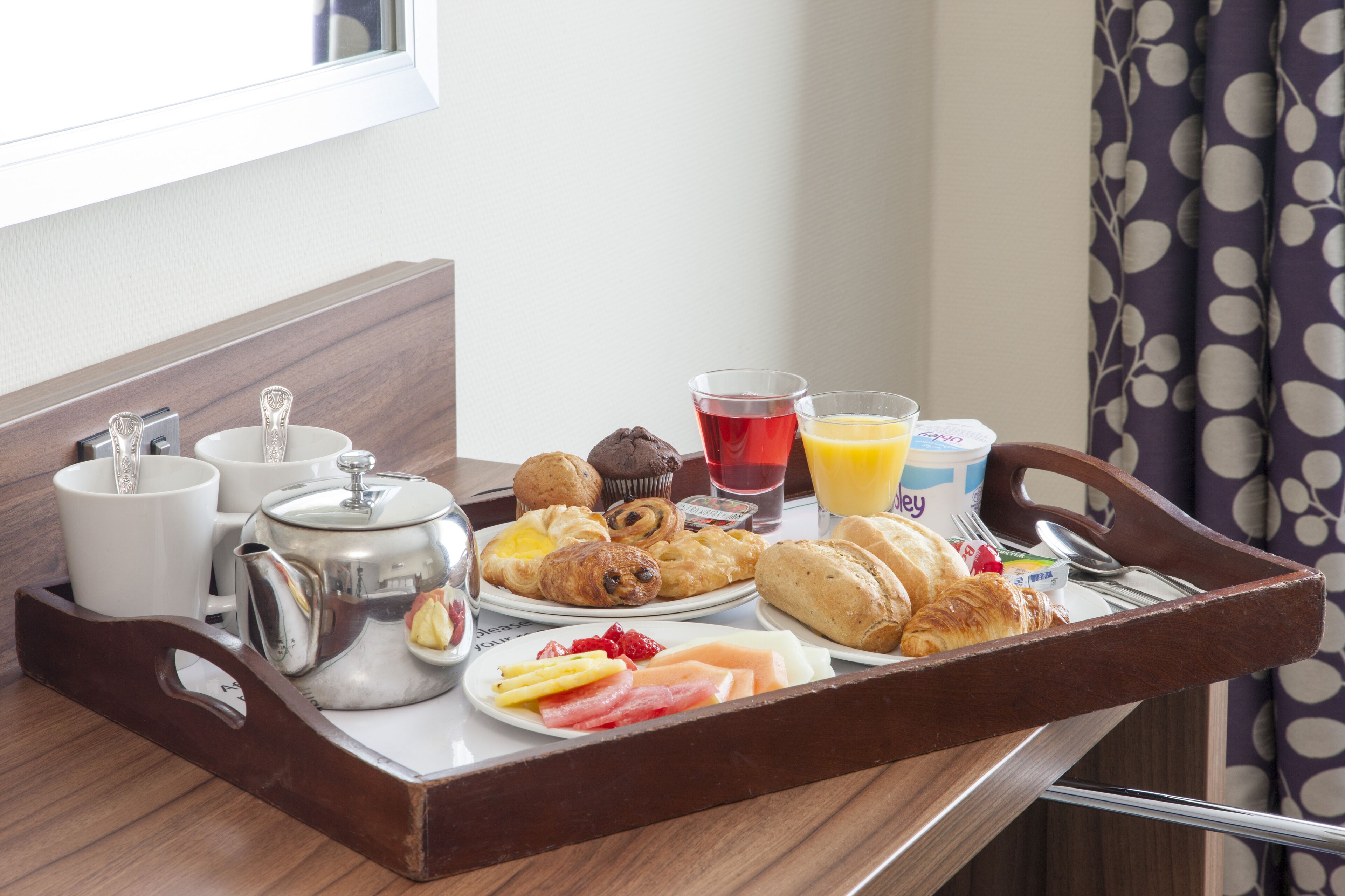 A breakfast tray with pastries, fruits, and beverages on a wooden table.