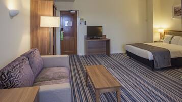 Habitación de hotel con sofá, cama, televisor sobre un mueble, una mesita y una lámpara.