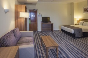Habitación de hotel con sofá, cama, televisor sobre un mueble, una mesita y una lámpara.