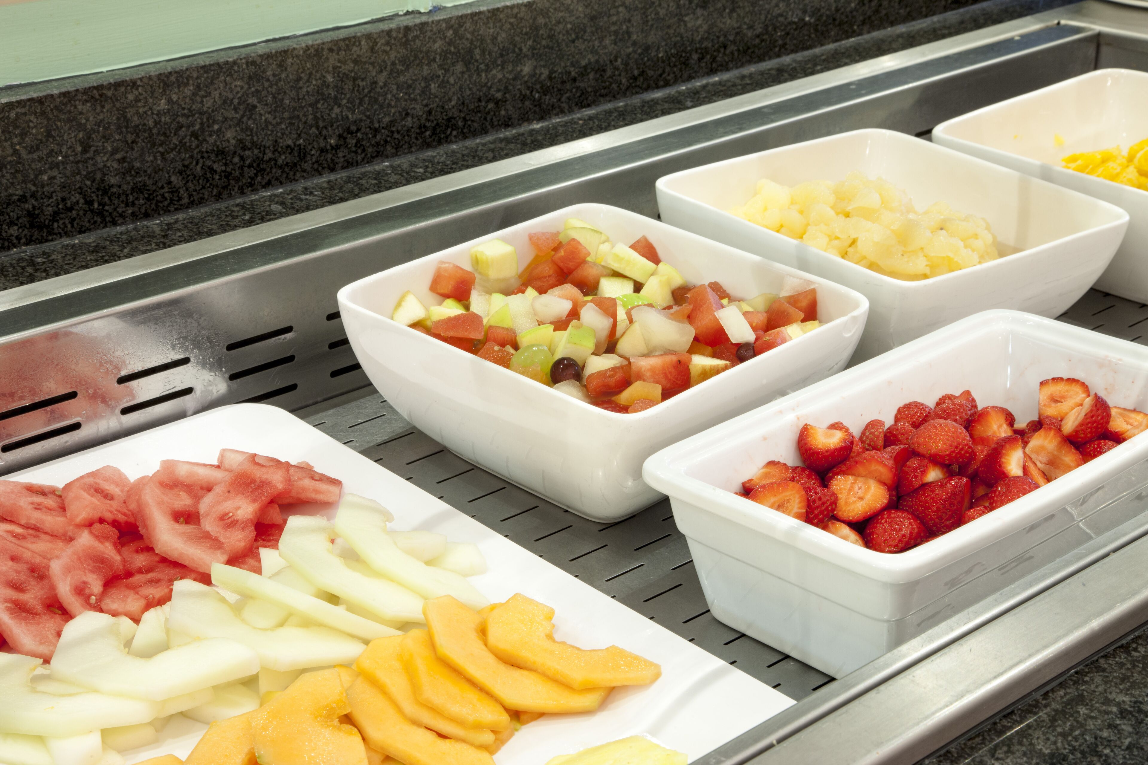 Un bufé con diversas frutas, incluyendo sandía, manzanas y fresas.