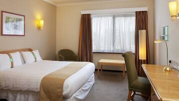 A hotel room with a large bed, a desk, a chair, a lamp, and a window with curtains.