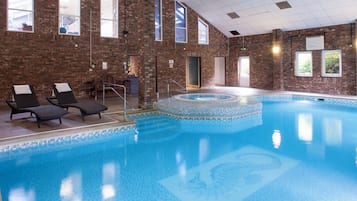 Ein Hallenbad mit gefliestem Rand, Liegestühlen und einer Ziegelwand.
