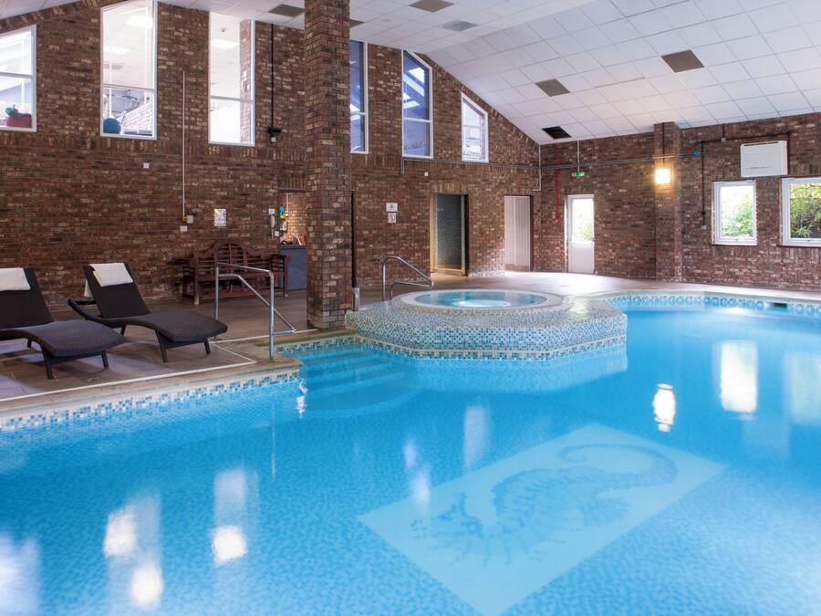 Ein Hallenbad mit gefliestem Rand, Liegestühlen und einer Ziegelwand.