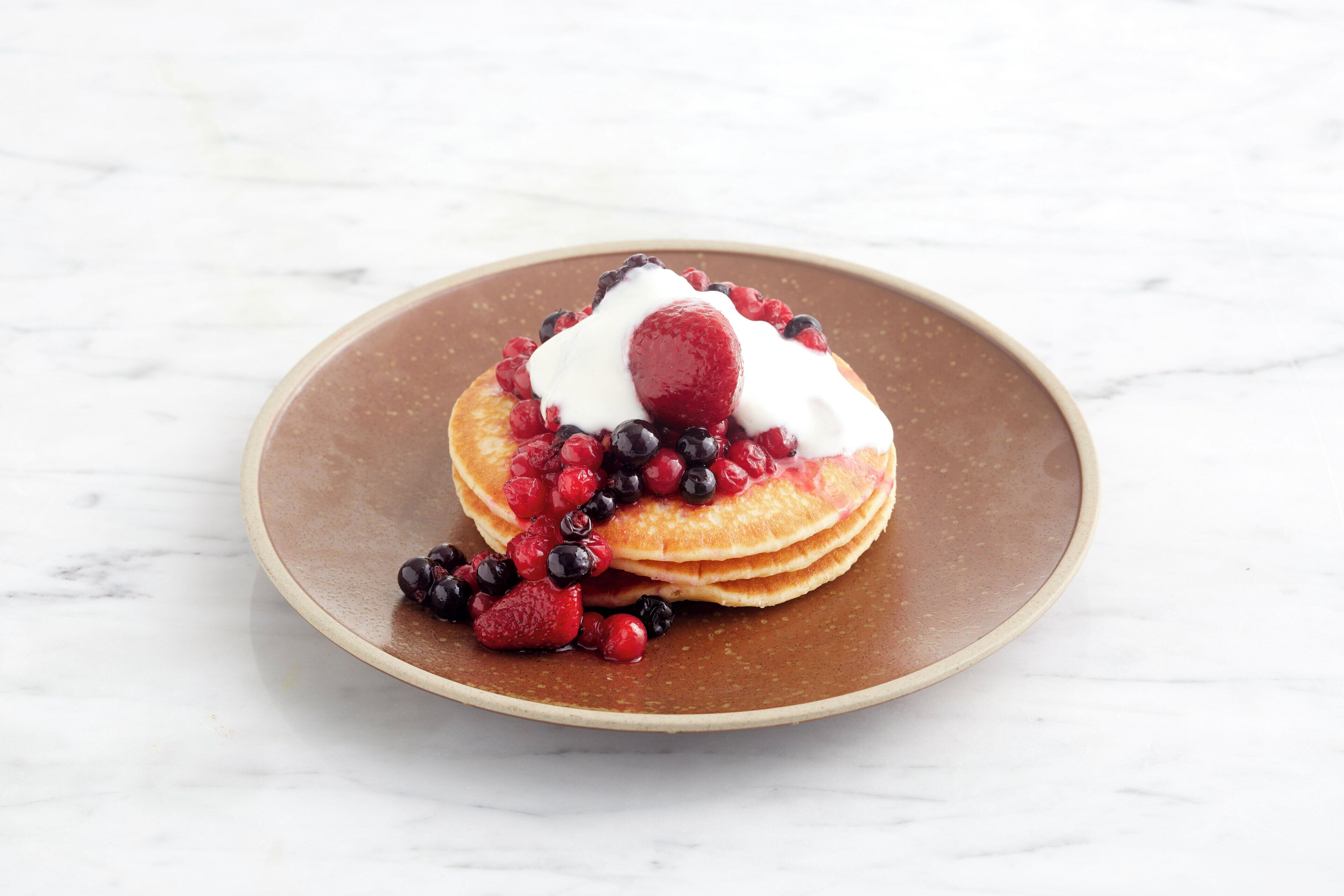 A stack of pancakes on a brown plate with berries and whipped cream.