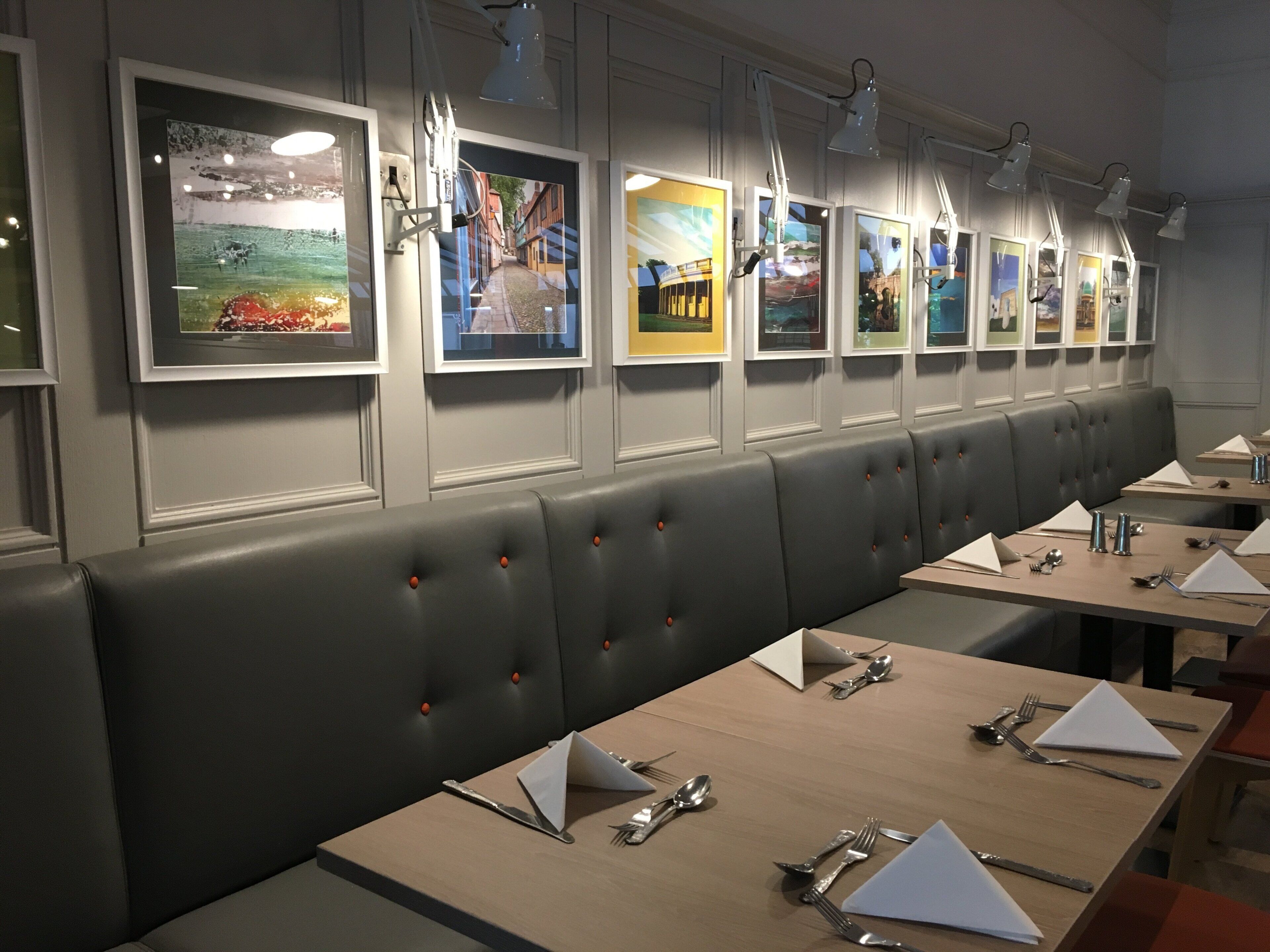 A restaurant with a long counter, multiple tables, and framed artwork on the wall.
