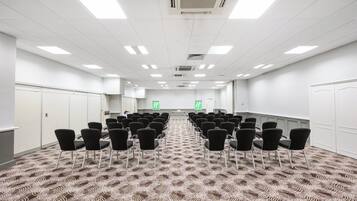 A conference room with rows of black chairs, a patterned carpet, white walls, and a white ceiling with lights.