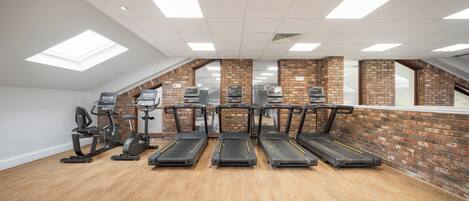 A gym with treadmills, elliptical machines, and stationary bikes arranged in a row.