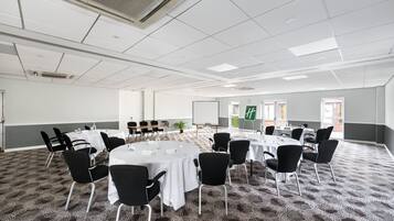 Un salón de conferencias con mesas redondas, sillas negras y piso alfombrado.