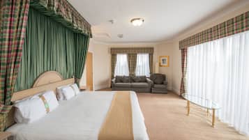 A hotel room with a large bed, a sofa, a glass coffee table, and curtains.
