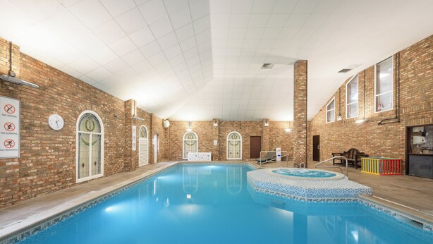 An indoor swimming pool with a brick wall, a hot tub, and a bench.