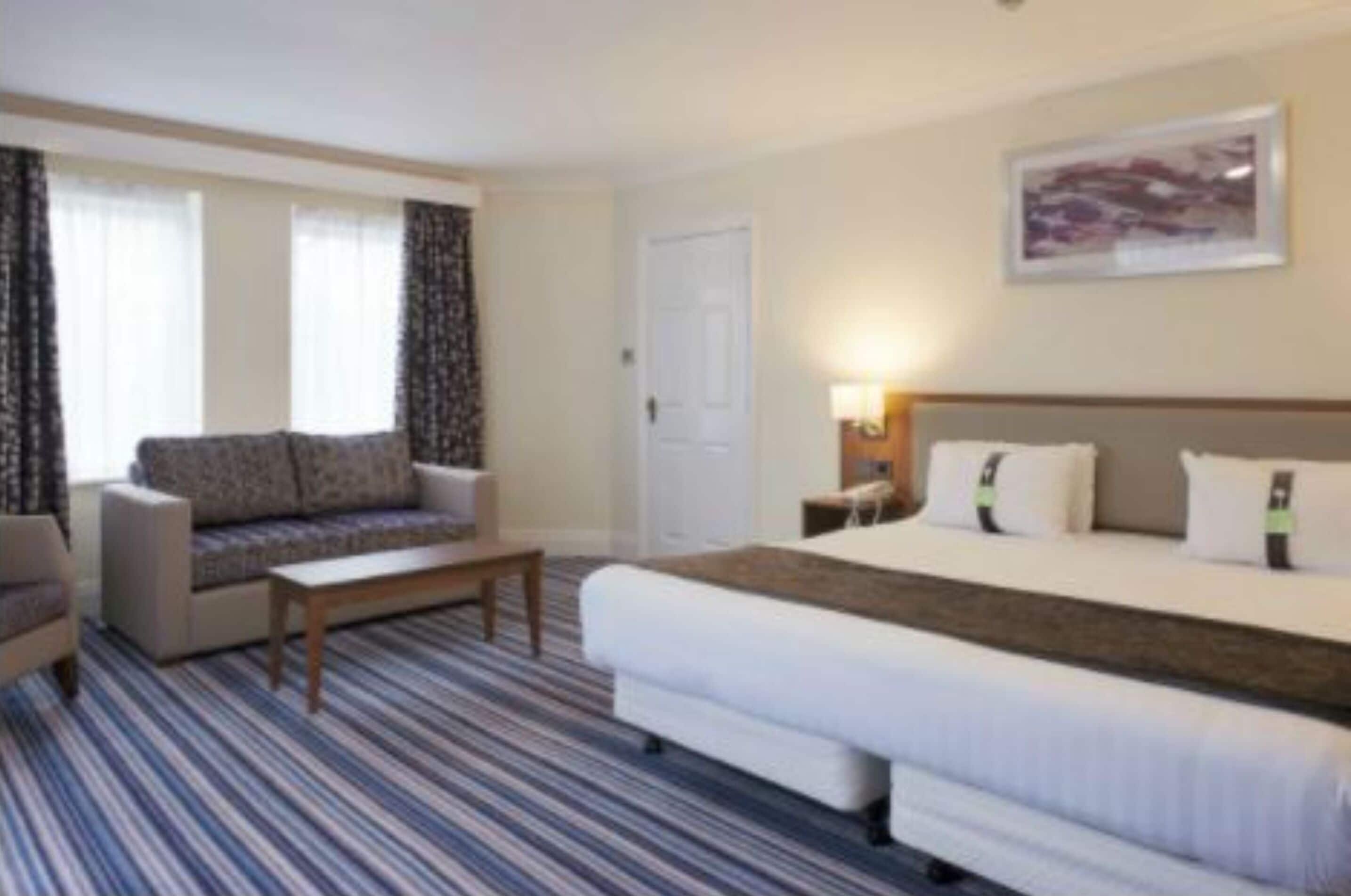 A hotel room with a bed, a sofa, a small table, and a window with curtains.