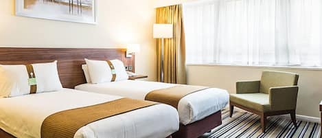 A hotel room with two beds, a desk, a chair, and a window with curtains.