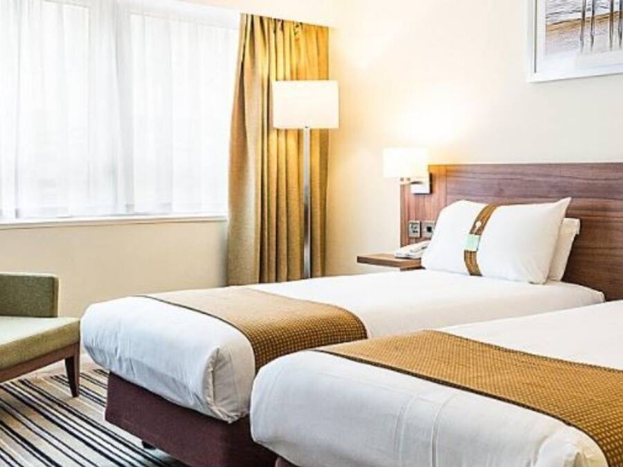 A hotel room with two beds, a desk, a chair, and a window with curtains.