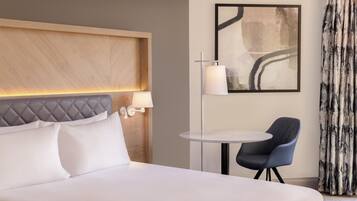 A hotel room with a large bed, a bedside table with a lamp, a chair, and a painting on the wall.
