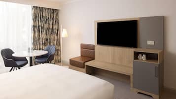 Una habitación de hotel con cama, televisor, escritorio y dos sillas, y un sofá.