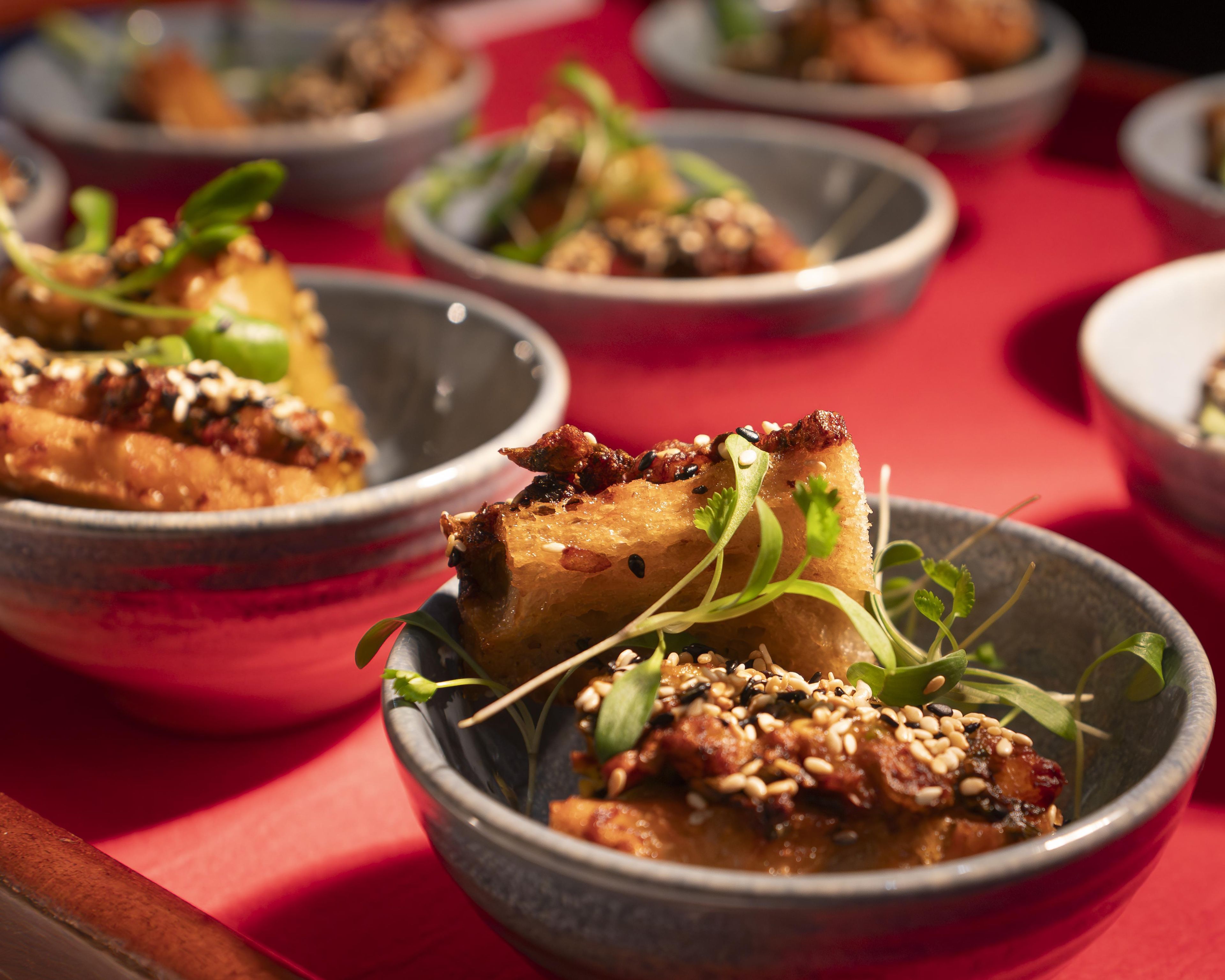 A series of dishes with a focus on a bowl containing a piece of food garnished with sesame seeds and greens.