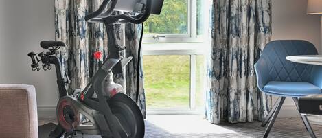 A Peloton stationary bike in a room with a large window, a blue chair, and a couch.