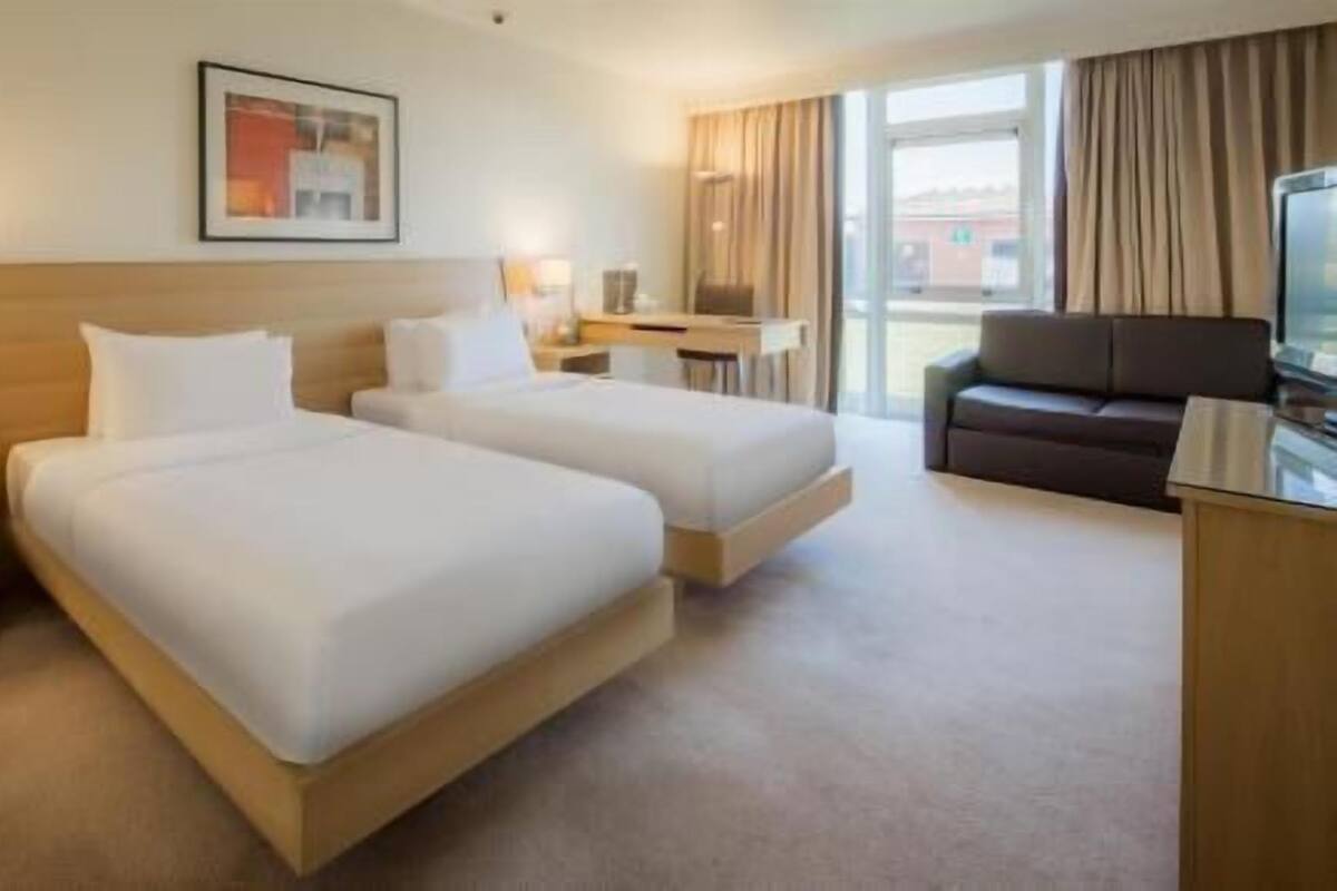 A hotel room with two beds, a desk, a television, and a window with curtains.