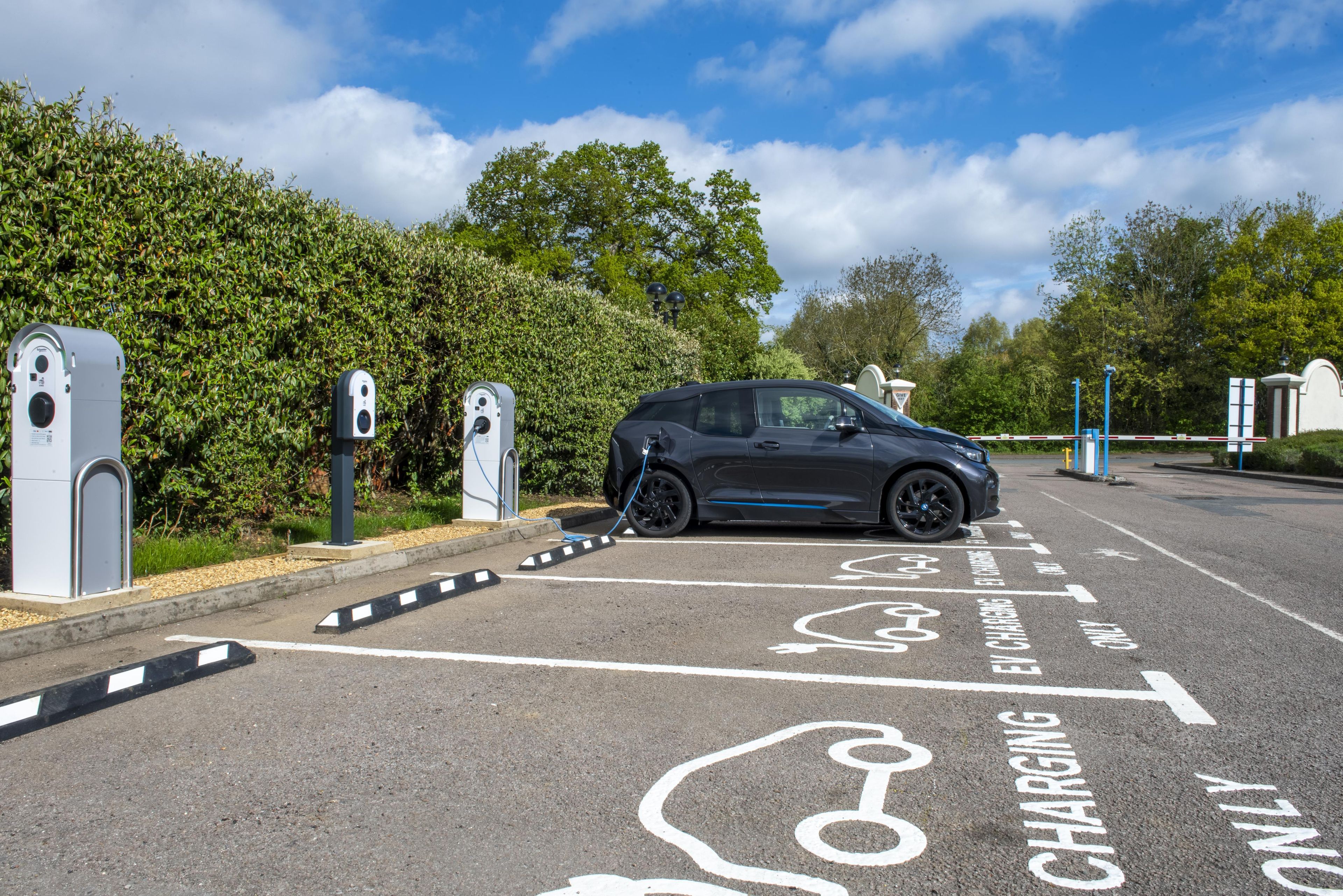 Un área de estacionamiento con estaciones de carga para vehículos eléctricos, un coche aparcado y cielo despejado.