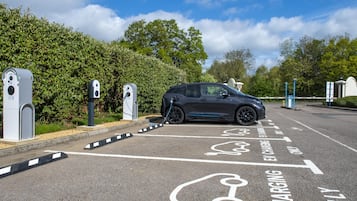 Un área de estacionamiento con estaciones de carga para vehículos eléctricos, un coche aparcado y cielo despejado.