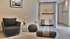 Una habitación moderna con un sillón oscuro, un banco acolchado, una planta en maceta y un cuadro en la pared.