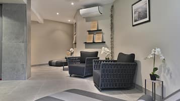 Un espacio de spa con dos sillones negros acolchados, una mesita pequeña y una orquídea en maceta.